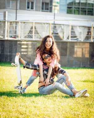 Yeşil çimenlerin üzerinde poz kaykay ile rahat kıyafetler'de iki genç karışık yarış kız