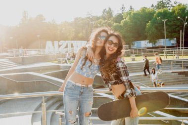 İki genç kız açık havada kaykay ile poz