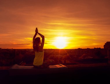 Genç kızı pratik Yoga çatıda. Gün batımında siluet.