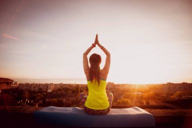Genç kızı pratik Yoga çatıda. Gün batımında siluet.