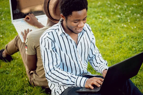 Two african students with laptops in green park.