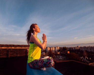 Genç kızı pratik Yoga çatıda. Gün batımında siluet.