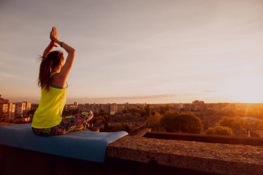 Genç kızı pratik Yoga çatıda. Gün batımında siluet.