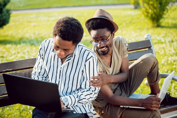 Two african students with laptops in green park.