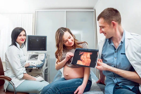 Female doctor and young pregnant woman patient with husband. Ultrasound equipment. Diagnostics. Sonography.