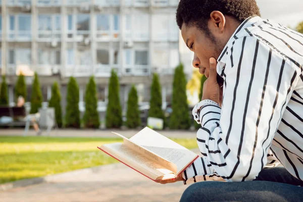 Young african man reading book in city park