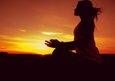 Genç kızı pratik Yoga çatıda. Gün batımında siluet.