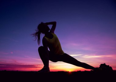 Genç kızı pratik Yoga çatıda. Gün batımında siluet.