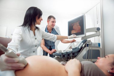 Kadın doktor ve kocası ile genç hamile kadın hasta. Ultrason cihazları. Tanılama. Ultrason.