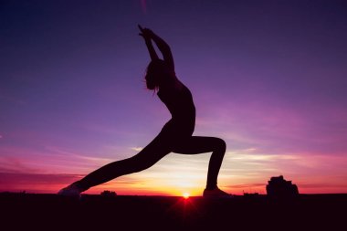 Genç kızı pratik Yoga çatıda. Gün batımında siluet.
