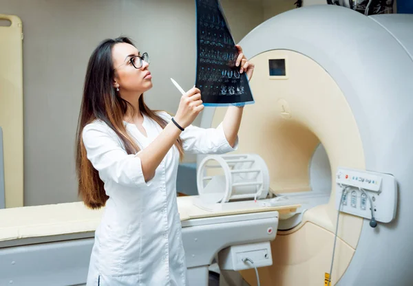 Young female middle eastern doctor looking at MRI picture. Medical equipment.