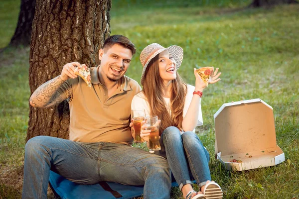 Happy couple on picnic in park. Eating pizza and drinking beer.