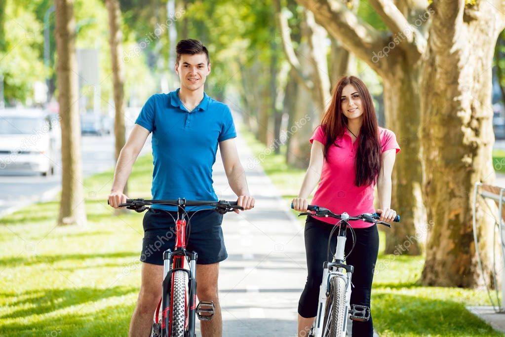 Young caucasian couple cycling on green bicycle lane in sunny day