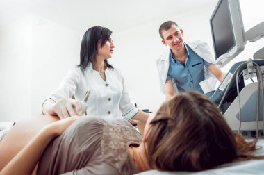 Kadın doktor ve kocası ile genç hamile kadın hasta. Ultrason cihazları. Tanılama. Ultrason.