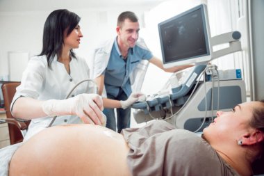 Kadın doktor ve kocası ile genç hamile kadın hasta. Ultrason cihazları. Tanılama. Ultrason.
