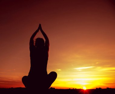 Genç kızı pratik Yoga çatıda. Gün batımında siluet.