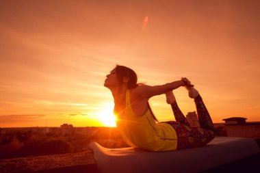 Genç kızı pratik Yoga çatıda. Gün batımında siluet.