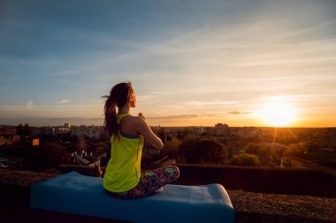 Genç kızı pratik Yoga çatıda. Gün batımında siluet.