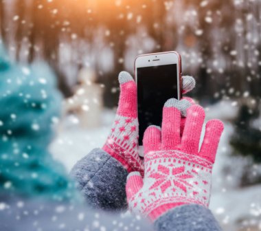 Smartphone ile pembe eldiven dokunmatik ekranlar için kışın kullanan kadın.