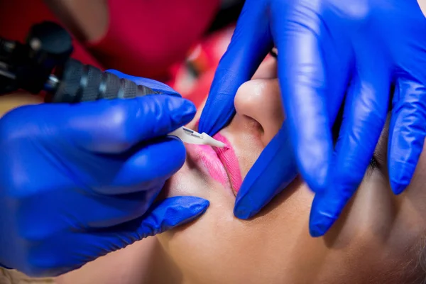 Professional tattooist makes the lips tattoo on a girl. Aesthetic medicine