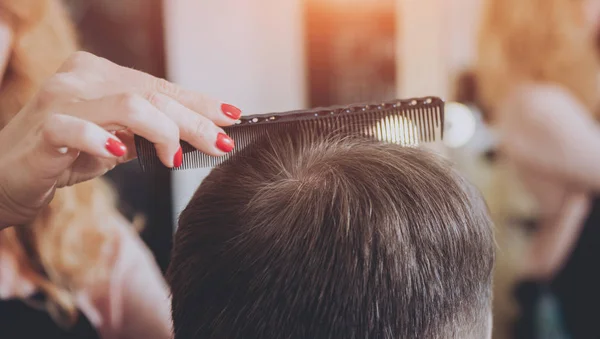 Hairdresser makes hairstyle for a young man.