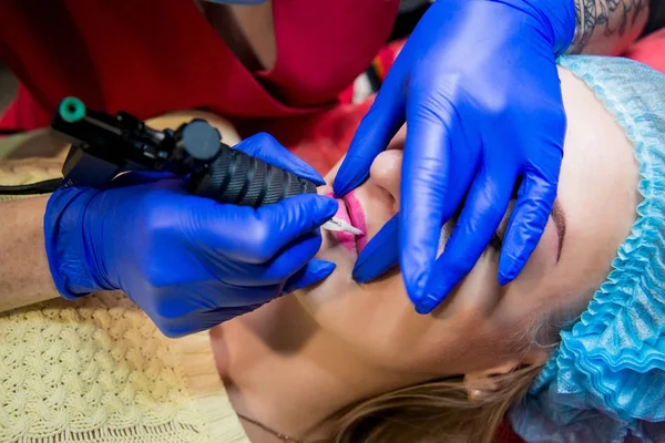 Professional tattooist makes the lips tattoo on a girl. Aesthetic medicine