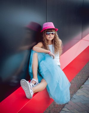 Küçük kız pembe şapka ve süslü mavi etek sokakta poz
