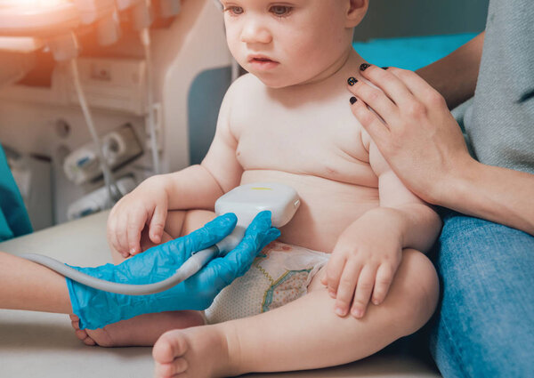 Doctor and infant girl with mother at ultrasound diagnosis. Medical equipment. Sonography.