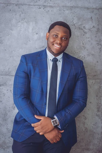 African american businessman in blue suit standing near the gray wall