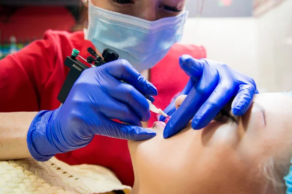 Professional tattooist makes the lips tattoo on a girl. Aesthetic medicine