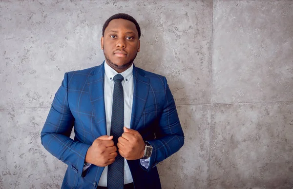 African american businessman in blue suit standing near the gray wall