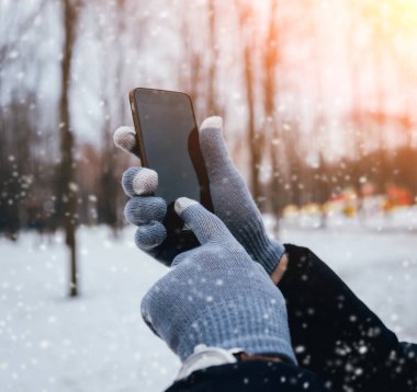 Smartphone ile gri eldiven dokunmatik ekranlar için kışın kullanan adam