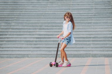 Güneşli bir gün, sokakta küçük kız sürme scooter