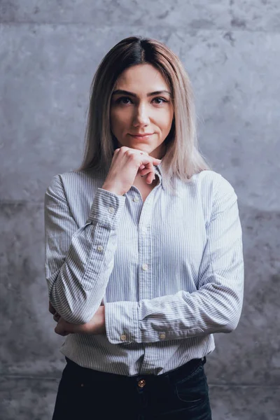 Attractive caucasian woman dressed in shirt posing before grey wall