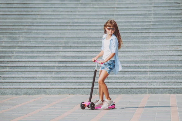Güneşli bir gün, sokakta küçük kız sürme scooter