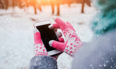 Smartphone ile pembe eldiven dokunmatik ekranlar için kışın kullanan kadın.