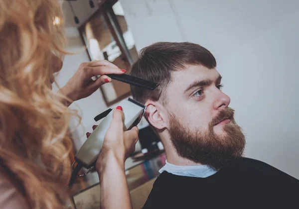 Hairdresser makes hairstyle for a young man.