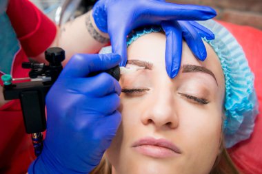 Profesyonel dövmeci kaş dövme bir kız yapar. Estetik tıp