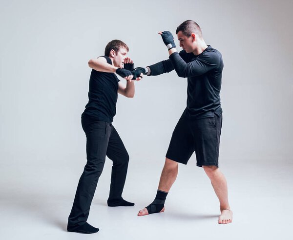 Young fighters practicing against a white wall in studio.