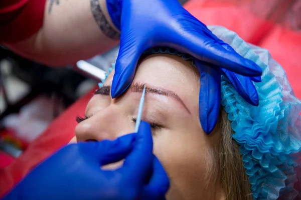 Professional tattooist makes the eyebrow tattoo on a girl. Aesthetic medicine