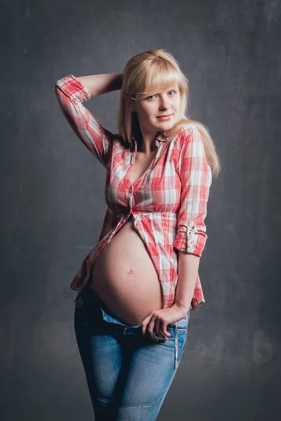 工作室图片美丽的怀孕的金发女郎在格子衬衫和蓝色牛仔裤 — 图库照片