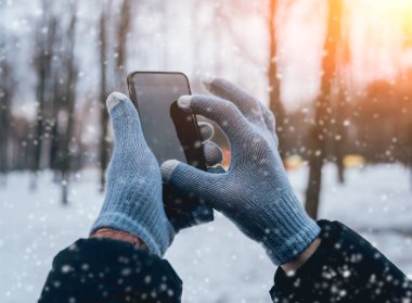 Smartphone ile gri eldiven dokunmatik ekranlar için kışın kullanan adam