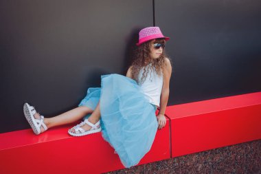 Küçük kız pembe şapka ve süslü mavi etek sokakta poz
