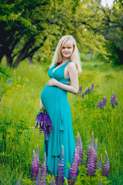 美丽的怀孕金发碧眼的妇女在公园的花朵 — 图库照片