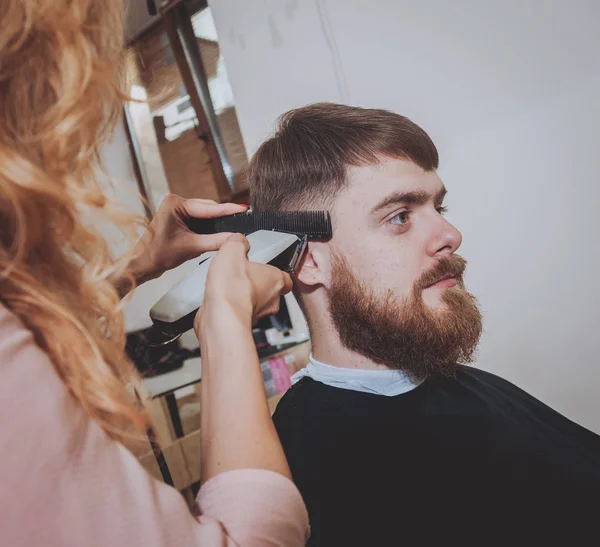 Master cuts hair and beard of men, hairdresser makes hairstyle for a young man.