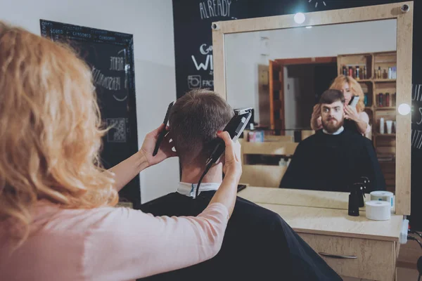 Master cuts hair and beard of men, hairdresser makes hairstyle for a young man.