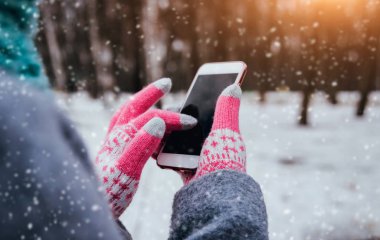 Smartphone ile pembe eldiven dokunmatik ekranlar için kışın kullanan kadın.