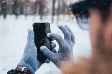 Smartphone ile gri eldiven dokunmatik ekranlar için kışın kullanan adam