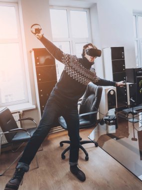 Mutlu genç adam ofiste bir oyun oynuyor. Sanal gerçeklik kulaklık.