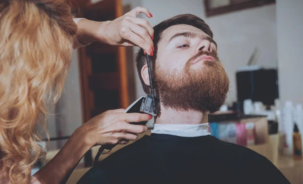 Master cuts hair and beard of men, hairdresser makes hairstyle for a young man.